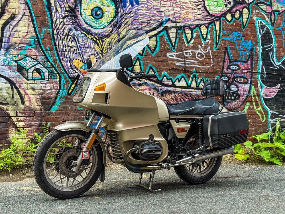 the gold-colored BMW R80RT parked in front of a brightly painted mural on a brick wall